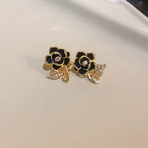 Close-up of elegant black rose stud earrings with gold edges and crystal leaf detail