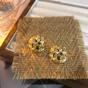 Vista detallada de pendientes dorados vintage con textura trenzada sobre fondo de arpillera