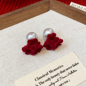 Elegant red flocked flower earrings with white pearl accents on minimalist fabric background