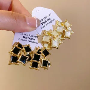 Close-up of geometric double-layer square stud earrings in gold and black enamel.