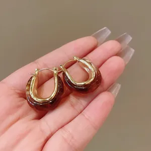 Detailed close-up of retro U-shaped geometric hoop earrings in gold and amber resin
