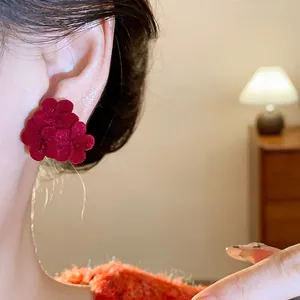 Close-up view of a red flocked flower earring worn on ear with soft warm indoor lighting