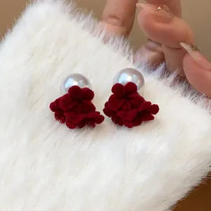 Macro view of red flocked flower and pearl stud earrings on white fur background