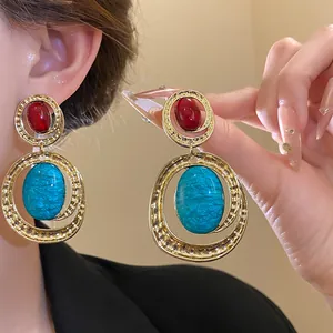Dettaglio di orecchini ovali vintage in oro con pietre di resina rosse e blu mare.