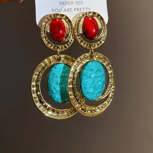 Dettaglio di orecchini vintage in oro con pietre ovali in resina rosse e turchesi