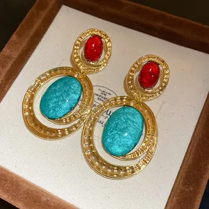 Dettaglio di orecchini vintage stile corte con resina rossa e turchese in finitura oro