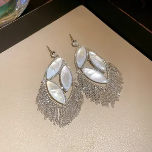 Close-up detail of oversized silver tassel earrings with mother of pearl and zircons