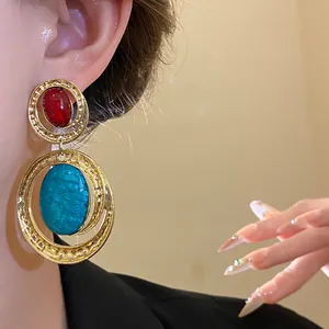 Orecchini vintage dorati con pietre ovali in resina rossa e blu petrolio su modella.