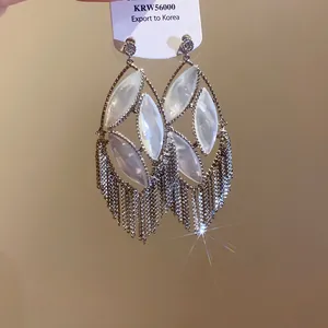 Detail view of oversized silver needle earrings with zircon, mother-of-pearl and tassel.