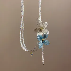 Detalle del collar de cuentas de cristal iridiscente con delicadas flores de malla azul y blanca.