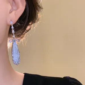 Close-up of silver dangling earring with zircon bow and teardrop mother-of-pearl