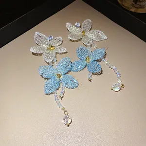 Detalle de delicadas joyas de flores tejidas en azul y blanco con borlas de cuentas