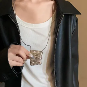 Dettaglio di un ciondolo a borsa intrecciata argento su una lunga collana a catena serpente.