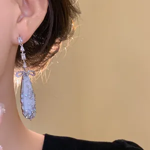 Close-up detail of elegant zircon and mother-of-pearl oval tassel earrings worn on ear