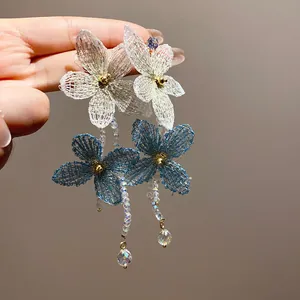 Primer plano de elegantes pendientes de flores tejidas en azul y blanco con borlas