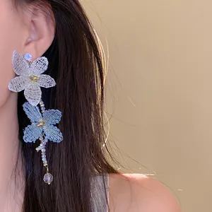 Primer plano de pendientes colgantes de flores de malla blancas y azules en una modelo asiática