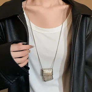 Dettaglio di una lunga collana maglione argento con ciondolo intrecciato quadrato.