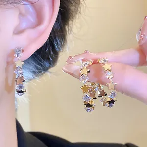 Dettaglio di orecchini a cerchio a C dorati con stelle in zircone scintillanti e chic