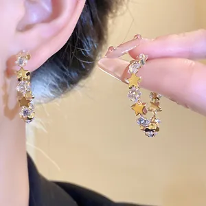 Primo piano di eleganti orecchini a C dorati con zirconi e stelle sull'orecchio