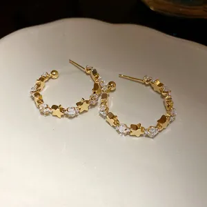 Dettaglio ravvicinato di orecchini a cerchio a C dorati con stelle e zirconi alternati.
