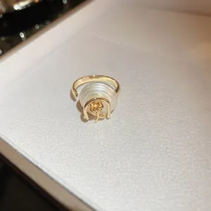 Détail d'une bague rose plaquée or avec perle sur fond de boîte à bijoux blanche.