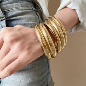 Détail rapproché d'un ensemble de joncs en métal doré épais porté au poignet avec chic.