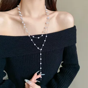 Detail showing a long French style pearl necklace worn over a black sweater.