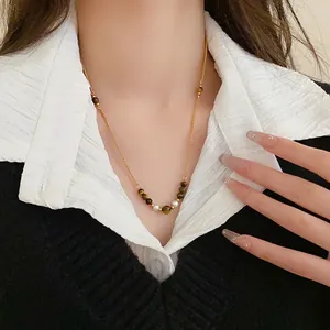 Elegante Detailaufnahme einer Halskette mit braunem Tigerauge und Perlen an einem Model.