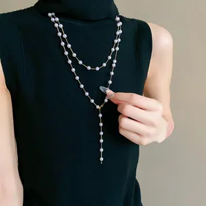 Detailed view of long French style artificial pearl necklace worn over black sweater.