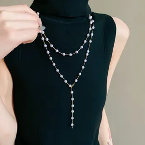 Detail view of a French style long faux pearl Y-necklace on a black turtleneck