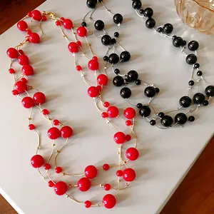 Close-up of elegant red and black artificial pearl layered necklaces with gold chain.