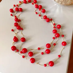 Detail view of long layered necklace with vibrant red faux pearls and gold chains.