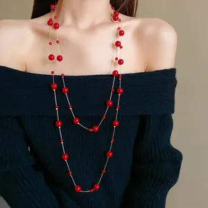 Elegant red faux pearl long necklace layered over a black sweater for a vintage look