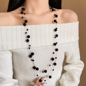 Detailed view of an elegant long black artificial pearl necklace on a white sweater.