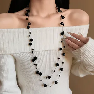 Elegant double-layered long black pearl necklace shown on a model wearing a white sweater.
