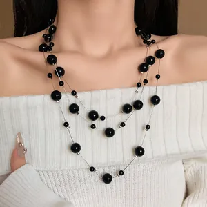 Detailed view of elegant multi-layered black pearl necklace on white knit sweater.
