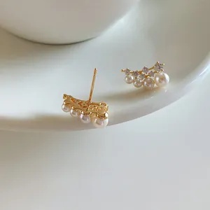 Elegant close-up of 18k gold plated silver needle stud earrings with pearls and zirconia stones.