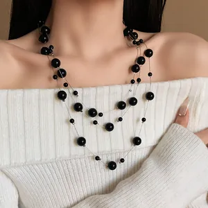 Elegant multi-layer black pearl necklace worn with white off-shoulder sweater.