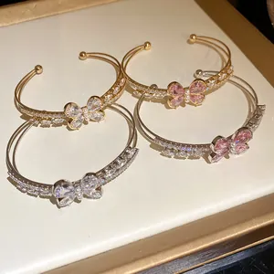 Detalle de pulseras abiertas de circonita con mariposa de doble capa en oro y plata