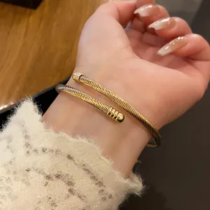 Detailed view of a golden twisted cable cuff bracelet on a wrist with elegant lace