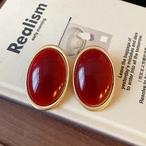 Close-up detail of vintage style oval red resin stud earrings with matte gold metal frame