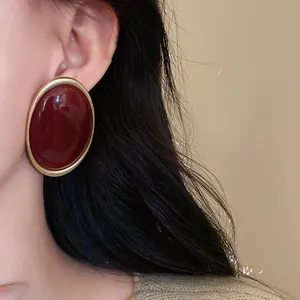 Close-up view of vintage palace style oval stud earrings with dark red center and gold trim