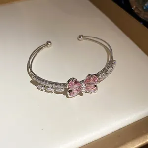 Detalle de un brazalete abierto de doble capa con un motivo de mariposa de circón rosa.
