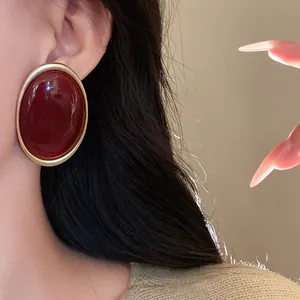 Vintage oval dark red stud earrings with gold trim worn by a model in a close-up shot