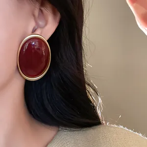 Close-up detail of vintage Ankora red oval stud earrings with a matte gold border on model