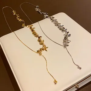 Detail of wheat ear tassel necklaces in gold and silver on a white jewelry display.