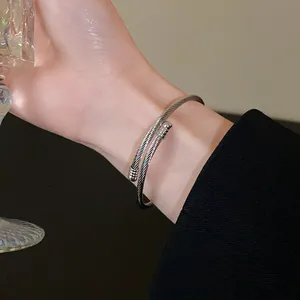 Close-up detail of silver twisted metal wire bangle on wrist with black blazer.