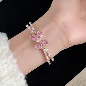 Vista detallada de un brazalete dorado de doble capa con una mariposa de circón rosa.