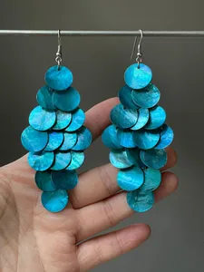 Détail de boucles d'oreilles pompons en nacre bleue avec disques circulaires superposés.