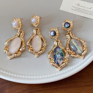 Close-up detail of retro oval shell stud earrings featuring gold textured frames and pearls